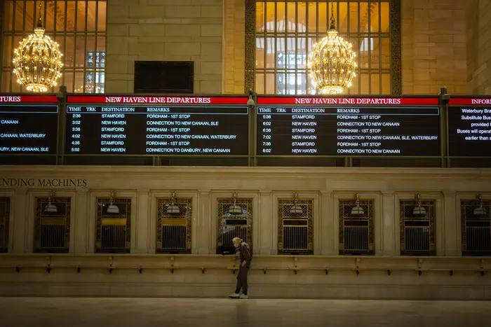 A lone man in a mask stands in front of Grand Central's ticketing booth.
